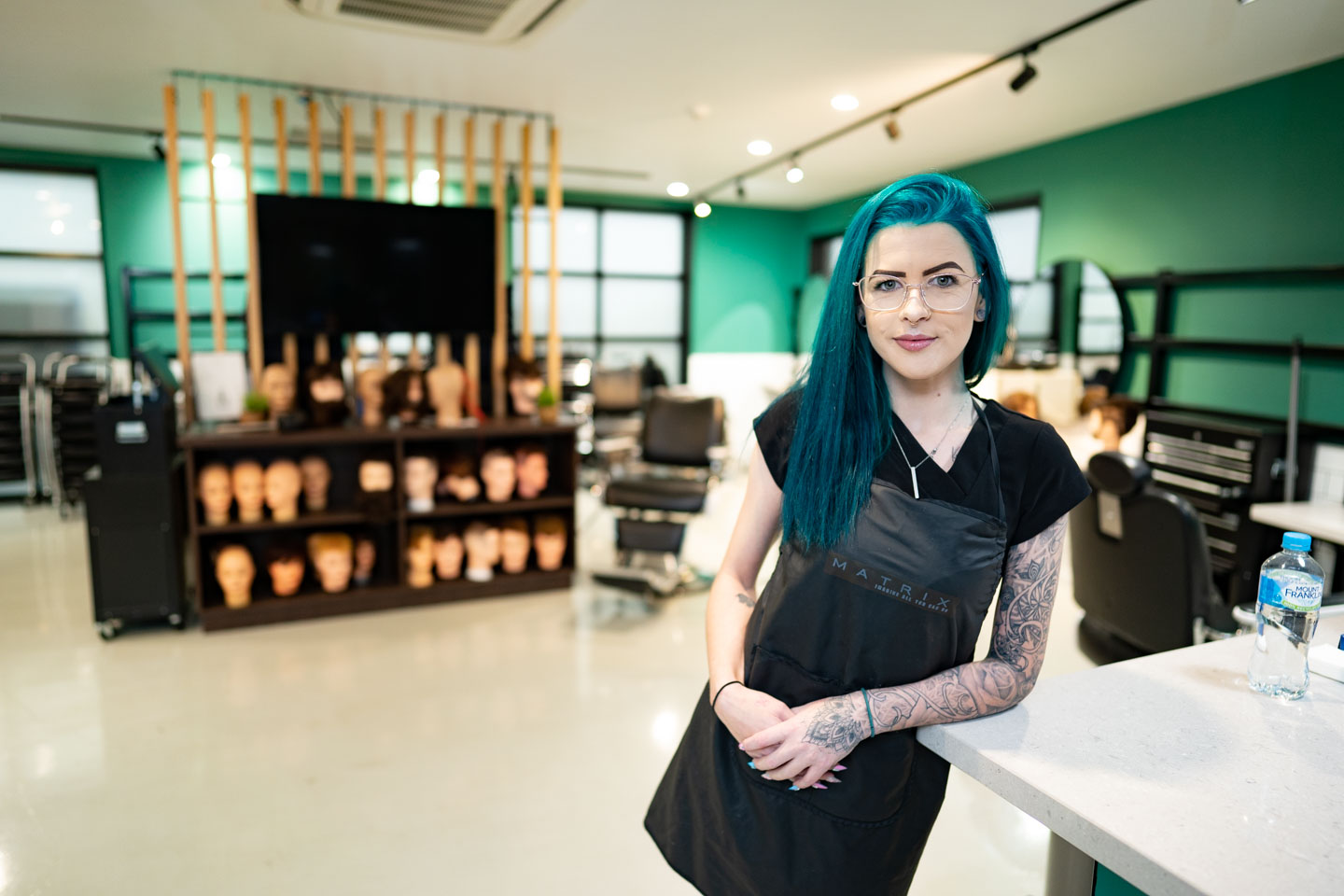 Young female student with blue hair learning and working in a haidressing salon.