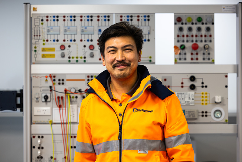 Mature-age, male, electrical trade apprentice standing in front of an electrical switchboard.